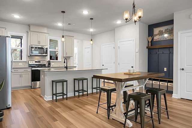 kitchen featuring a center island with sink, stainless steel appliances, light wood-style floors, a sink, and a kitchen breakfast bar