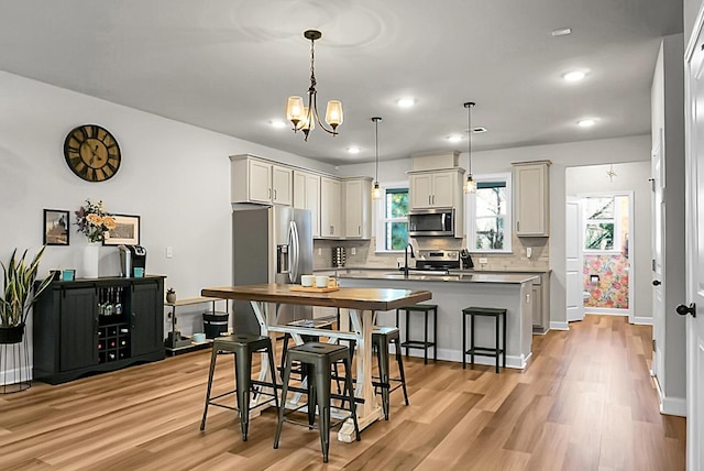 kitchen featuring a breakfast bar area, appliances with stainless steel finishes, backsplash, light wood finished floors, and an island with sink