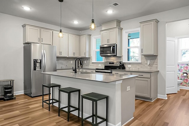 kitchen with light wood finished floors, visible vents, a breakfast bar, stainless steel appliances, and a sink