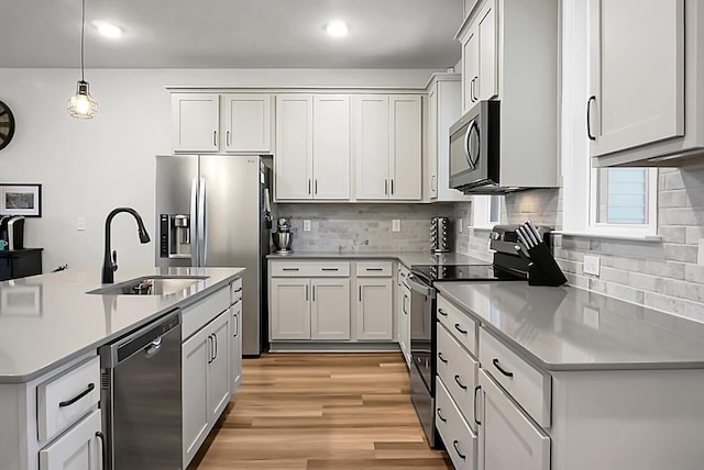 kitchen with stainless steel appliances, a sink, light countertops, light wood-type flooring, and decorative light fixtures