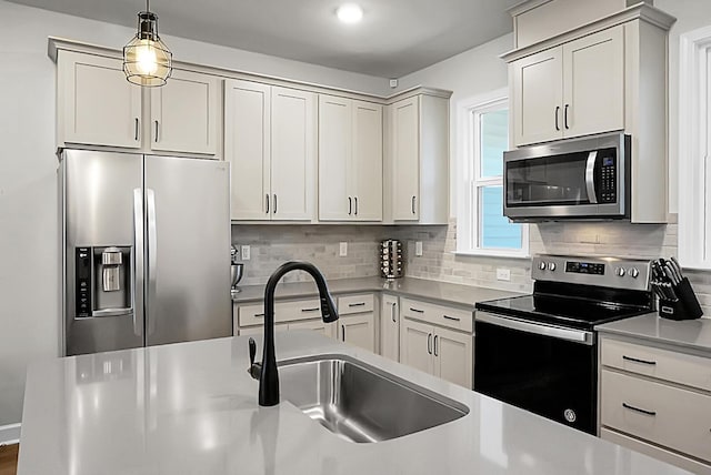 kitchen featuring decorative backsplash, appliances with stainless steel finishes, light countertops, pendant lighting, and a sink