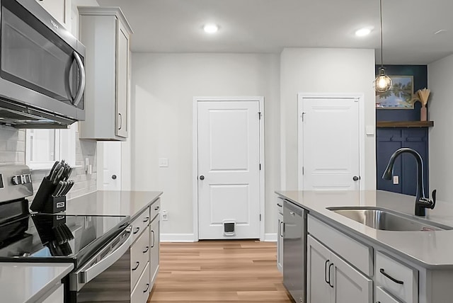 kitchen with stainless steel appliances, a sink, light countertops, light wood-type flooring, and pendant lighting