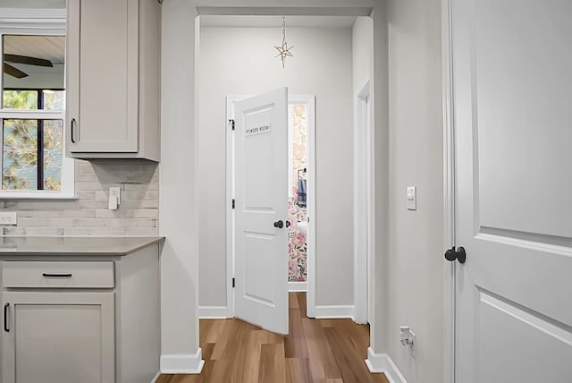 interior space featuring tasteful backsplash, light countertops, a ceiling fan, wood finished floors, and baseboards