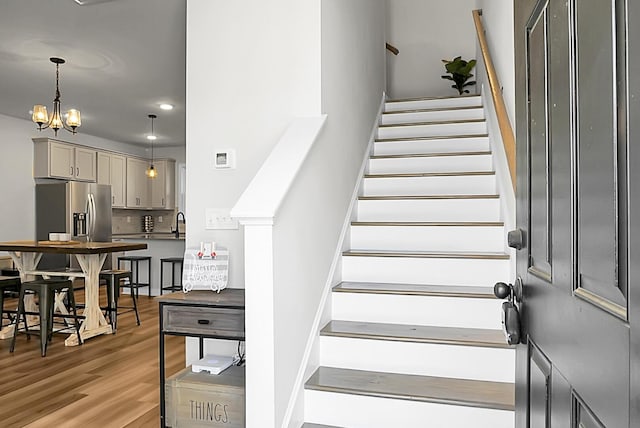 stairs featuring wood finished floors and a notable chandelier