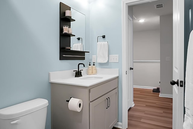 bathroom with toilet, wood finished floors, vanity, visible vents, and baseboards