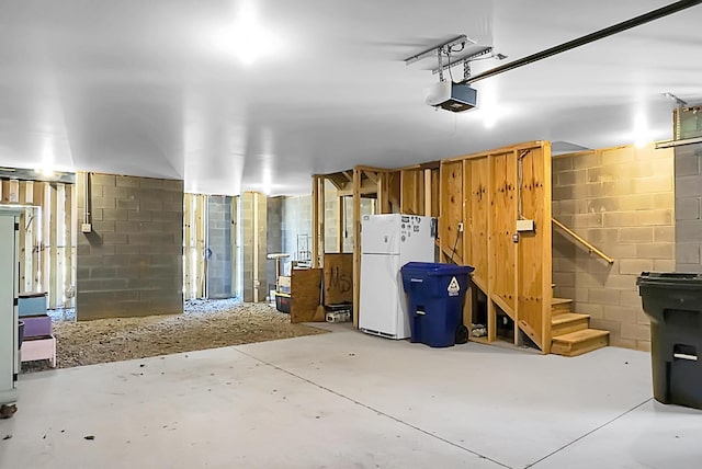 garage with concrete block wall, freestanding refrigerator, and a garage door opener