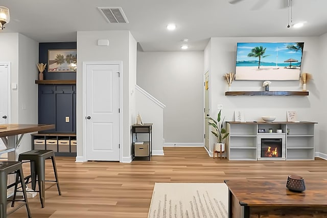 interior space featuring light wood-type flooring, a glass covered fireplace, visible vents, and baseboards