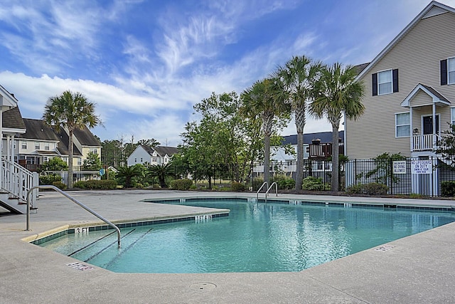 community pool with a patio area, fence, and a residential view