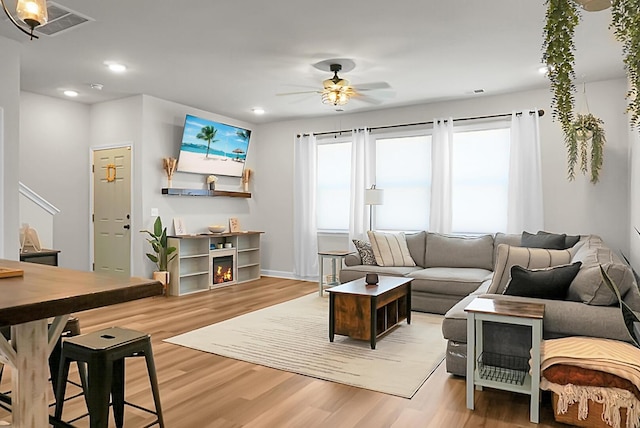 living area featuring recessed lighting, visible vents, ceiling fan, wood finished floors, and a warm lit fireplace