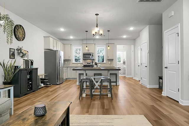 kitchen featuring light wood-style flooring, stainless steel appliances, a kitchen island, dark countertops, and a kitchen bar