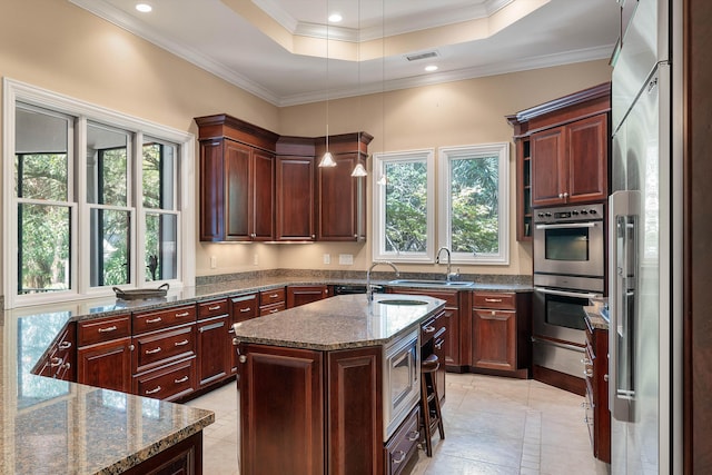 kitchen with pendant lighting, stainless steel appliances, a center island with sink, and a wealth of natural light