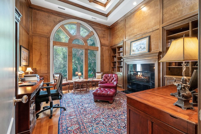 office space featuring a high ceiling, crown molding, built in shelves, and hardwood / wood-style floors