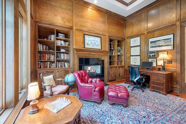 home office featuring wood walls, crown molding, built in features, wood-type flooring, and a tiled fireplace