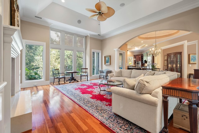 living room featuring a raised ceiling, a high ceiling, ceiling fan with notable chandelier, and light wood-type flooring