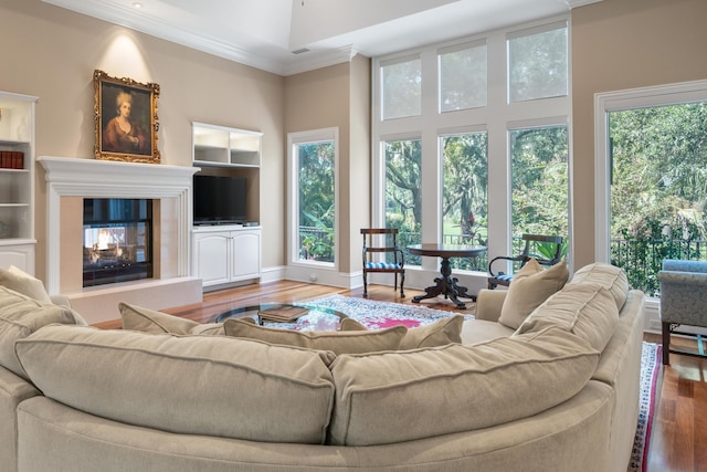 living room with hardwood / wood-style floors, a towering ceiling, crown molding, and built in shelves