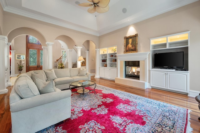 living room with a multi sided fireplace, hardwood / wood-style flooring, ceiling fan, ornate columns, and ornamental molding