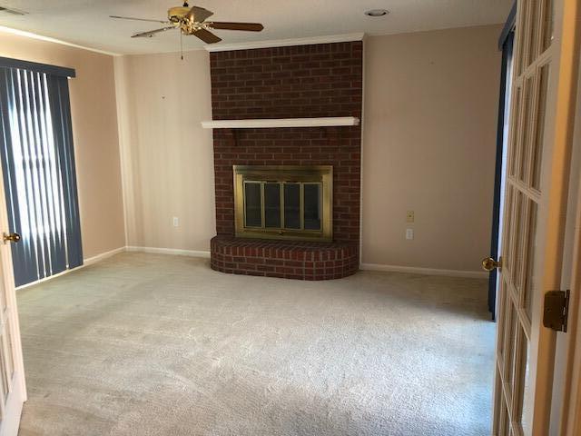 unfurnished living room with a brick fireplace, light colored carpet, and ceiling fan