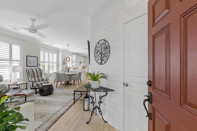 foyer with ornamental molding, light wood-style flooring, ceiling fan, and visible vents
