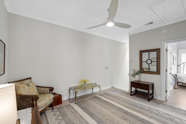 living area with visible vents, ornamental molding, a ceiling fan, light wood finished floors, and attic access