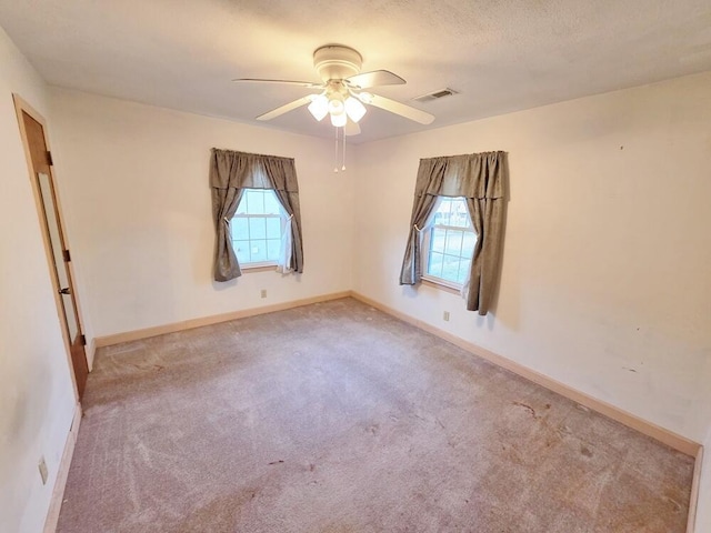 carpeted spare room with baseboards, visible vents, ceiling fan, and a textured ceiling