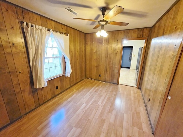 unfurnished room with wooden walls, visible vents, ceiling fan, and light wood-style flooring