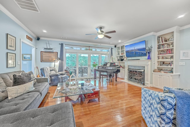 living room with a high end fireplace, built in features, light wood-type flooring, ceiling fan, and crown molding