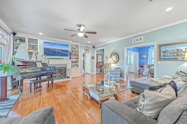 living room with built in shelves, light hardwood / wood-style flooring, ceiling fan, and ornamental molding