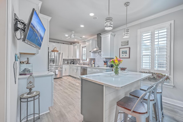 kitchen with wall chimney exhaust hood, decorative light fixtures, a kitchen bar, white cabinetry, and stainless steel appliances