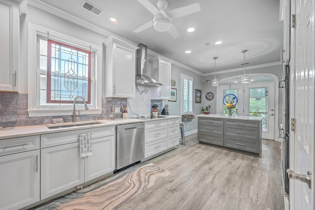 kitchen with stainless steel dishwasher, pendant lighting, sink, wall chimney exhaust hood, and light wood-type flooring