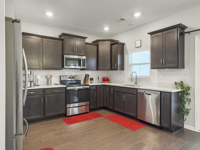 kitchen with stainless steel appliances, a sink, decorative backsplash, dark wood-style floors, and recessed lighting