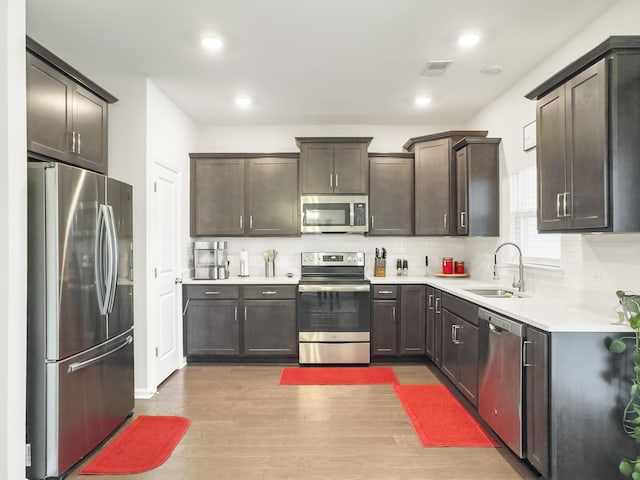 kitchen with stainless steel appliances, a sink, wood finished floors, dark brown cabinetry, and recessed lighting