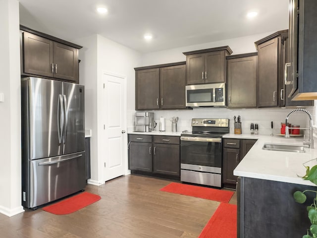 kitchen with stainless steel appliances, a sink, dark brown cabinets, dark wood-style flooring, and baseboards