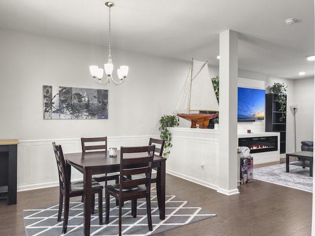 dining room featuring a decorative wall, wood finished floors, a chandelier, a glass covered fireplace, and a wainscoted wall