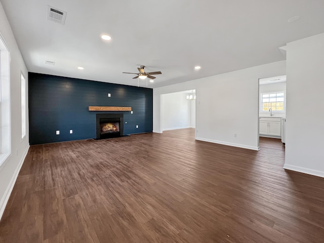 unfurnished living room featuring a warm lit fireplace, an accent wall, dark wood-style flooring, a sink, and visible vents