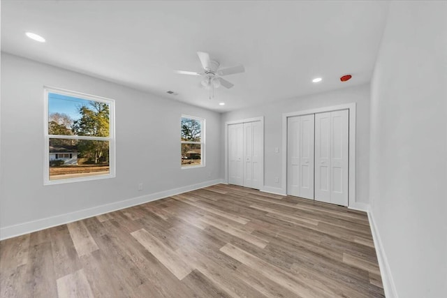 unfurnished bedroom with two closets, ceiling fan, and light hardwood / wood-style flooring