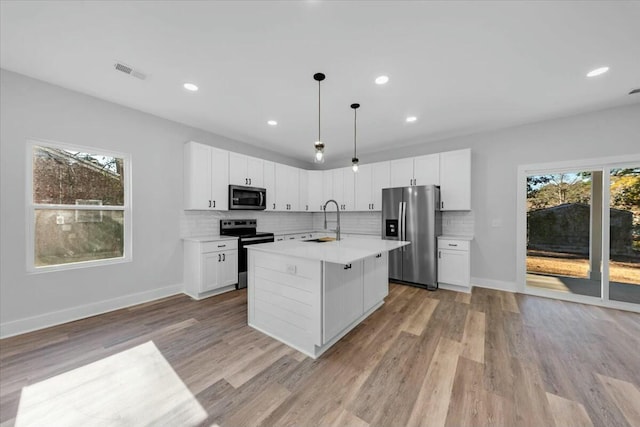 kitchen with hanging light fixtures, stainless steel appliances, a center island with sink, white cabinets, and sink