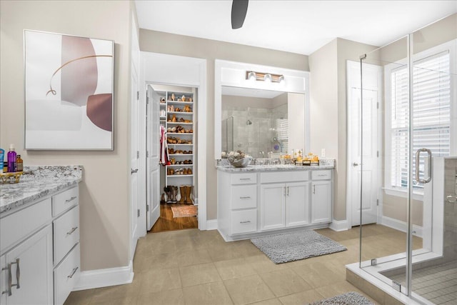 bathroom featuring a shower stall, two vanities, a spacious closet, baseboards, and tile patterned flooring