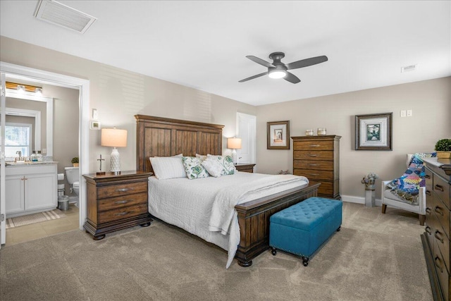 bedroom featuring light colored carpet, ensuite bathroom, ceiling fan, and baseboards
