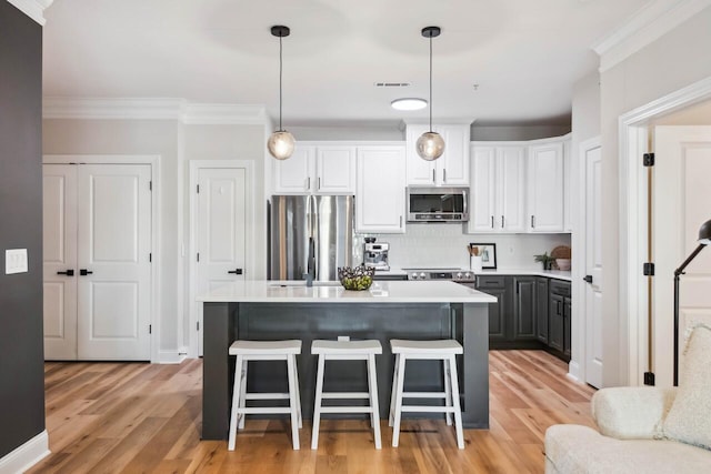 kitchen with white cabinetry, stainless steel appliances, decorative light fixtures, and light wood-type flooring