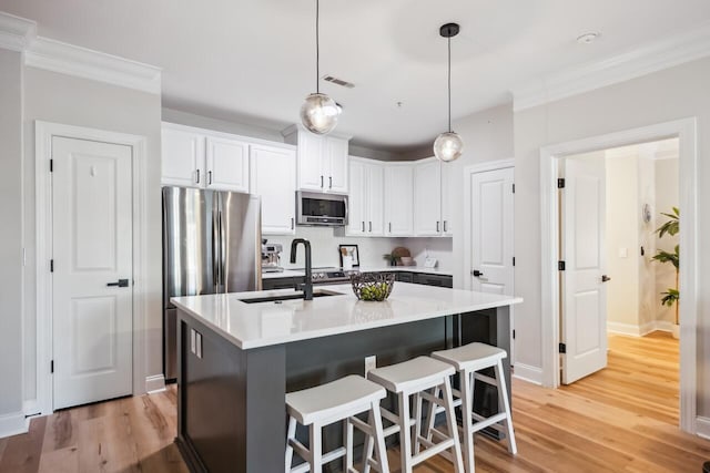 kitchen with decorative light fixtures, white cabinets, a kitchen island with sink, light hardwood / wood-style floors, and stainless steel appliances