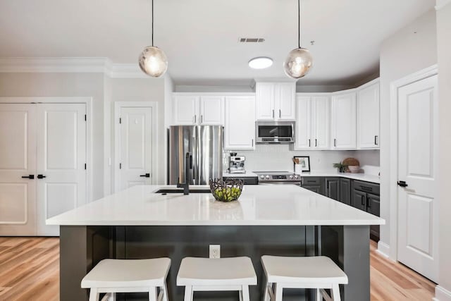 kitchen featuring hanging light fixtures, white cabinetry, appliances with stainless steel finishes, and a center island with sink