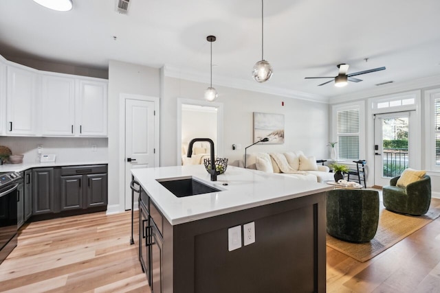 kitchen featuring an island with sink, sink, white cabinets, hanging light fixtures, and light hardwood / wood-style flooring