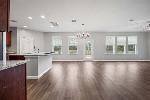 kitchen with ceiling fan with notable chandelier, decorative light fixtures, a kitchen bar, light stone countertops, and dark wood-type flooring