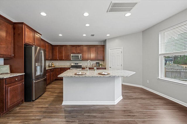 kitchen featuring sink, appliances with stainless steel finishes, dark hardwood / wood-style flooring, an island with sink, and light stone countertops