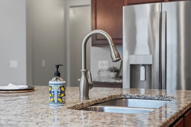 interior details with light stone countertops, sink, and stainless steel fridge