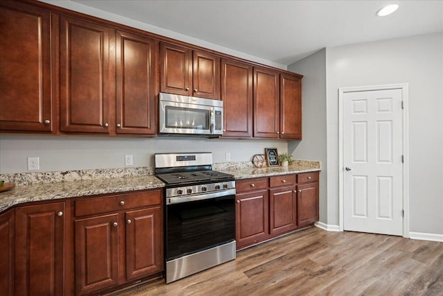 kitchen featuring stainless steel appliances, light stone countertops, and wood-type flooring