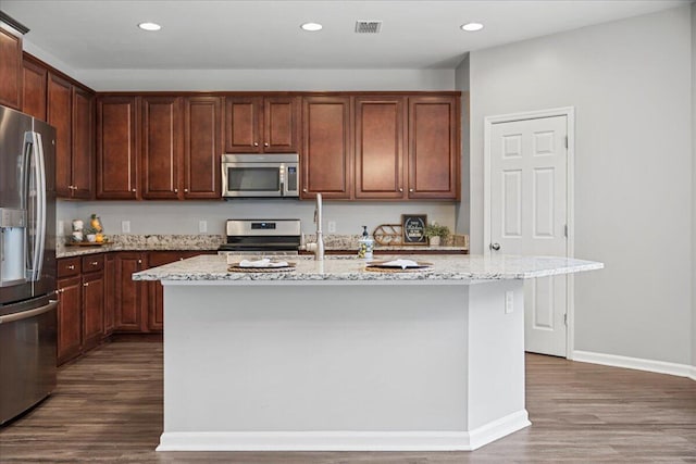 kitchen featuring light stone counters, dark wood-type flooring, an island with sink, and appliances with stainless steel finishes