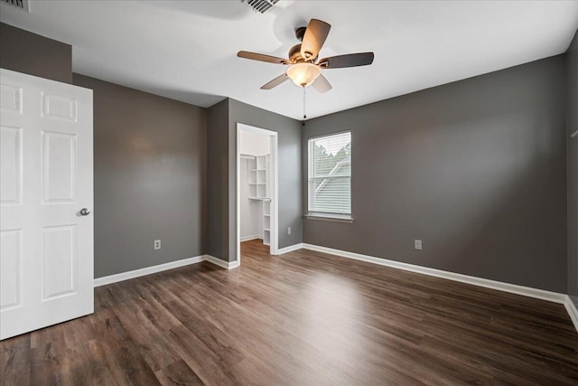 unfurnished bedroom with a walk in closet, dark wood-type flooring, a closet, and ceiling fan