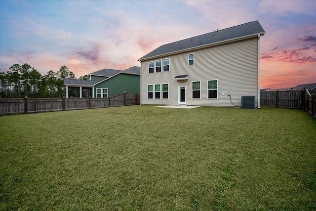 back house at dusk featuring a yard, a patio, and central air condition unit