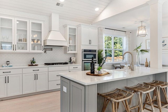 kitchen with a breakfast bar, custom range hood, double oven, white cabinetry, and gas cooktop